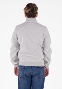 Giacca a vento grigia chiara con colletto alto, polsini ed elastico in vita, caratterizzata da una texture liscia e un design minimalista.