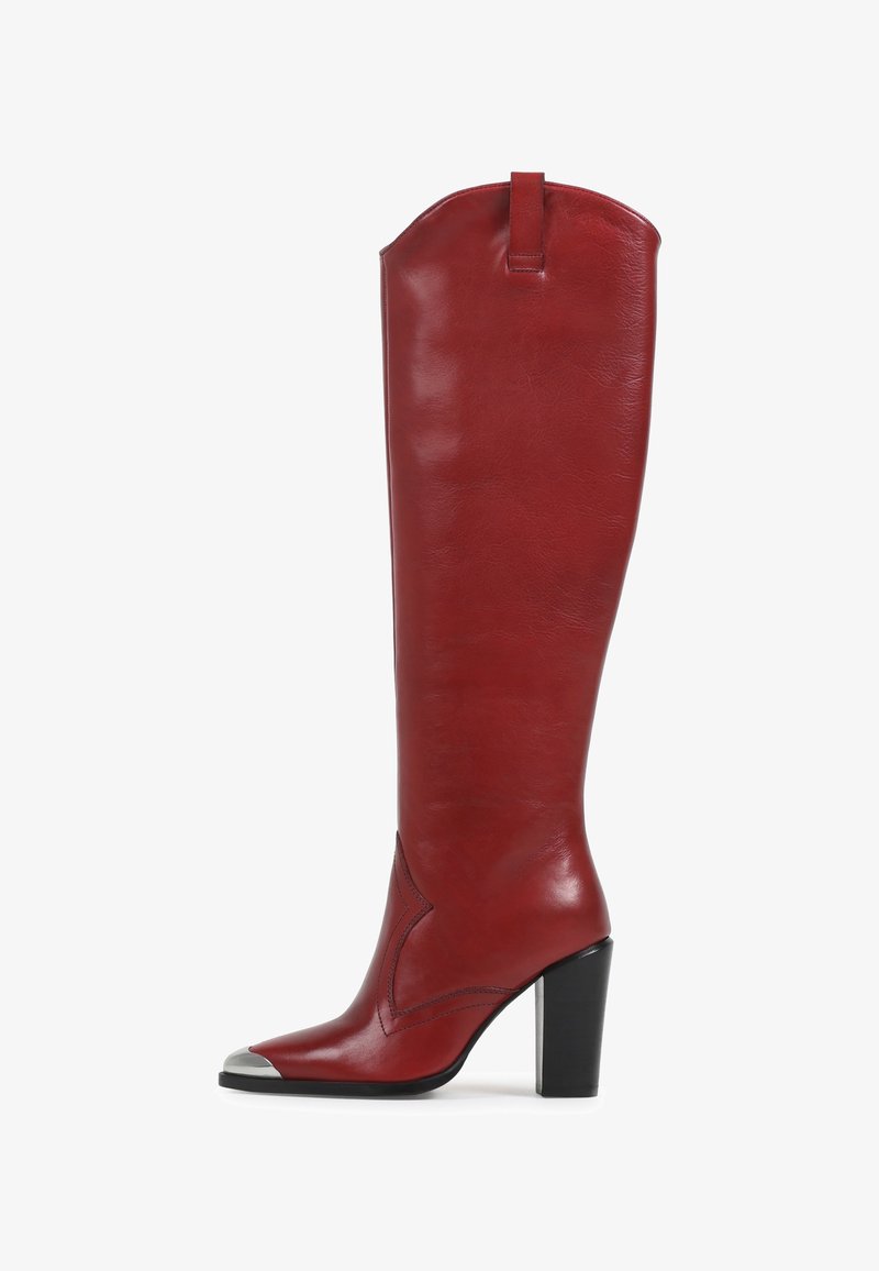 Bota de couro vermelha até ao joelho com bico pontudo, biqueira em prata e um salto bloco de altura média. Apresenta uma textura suave e costuras decorativas.