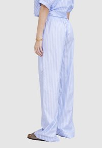 Hellblaue gestreifte Baumwollhose mit lockerer Passform und elastischem Bund, kombiniert mit lässigem Schuhwerk.