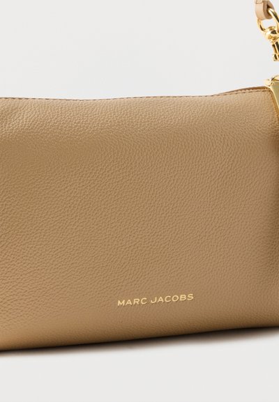Μπεζ τσαντάκι από δερμάτινη υφή με χρυσό φερμουάρ, χρυσό λουράκι αλυσίδα και ανάγλυφη επιγραφή "Marc Jacobs" με χρυσά γράμματα μπροστά.