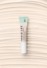 Siero per gli occhi Awakening di Indie Lee in un tubo trasparente con un cappuccio azzurro chiaro. Il design minimalista presenta testo bianco su uno sfondo beige.