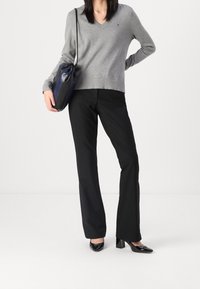 Un pull gris à col en V, un pantalon noir ajusté et des escarpins noirs brillants. Un sac structuré bleu marine complète la tenue. Texture lisse tout au long.