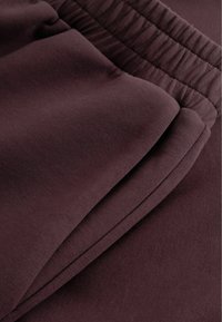 Bordeaux joggers med en glat tekstur og elastisk talje, der har sidelommer og en afslappet pasform. Detaljeret syning langs sømmene.