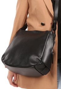 Zwarte leren handtas met een gestructureerde afwerking, slungelige vorm, verstelbare schouderriem en een ritsvak aan één kant.