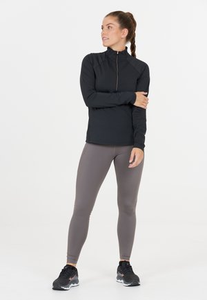 Sort zip-up sportstrøje med lange ærmer, parret med lysegrå leggings. Har et strømlinet design og ydeevne stof. Sorte sneakers fuldender looket.