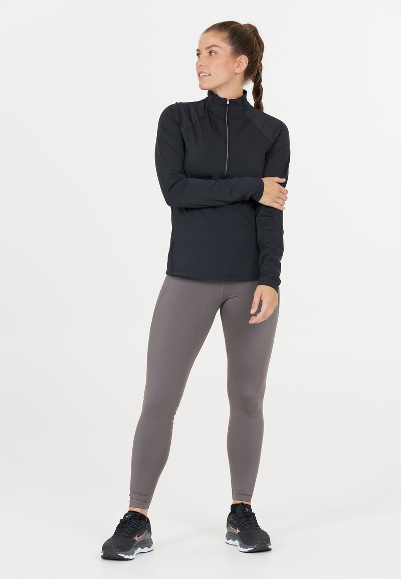 Sort zip-up sportstrøje med lange ærmer, parret med lysegrå leggings. Har et strømlinet design og ydeevne stof. Sorte sneakers fuldender looket.