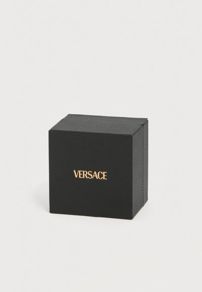 Μαύρο κουτί Versace με χρυσό λογότυπο στο κέντρο, σε απλό ανοιχτό γκρι φόντο.