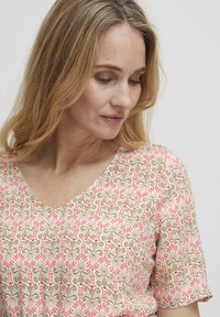 Blouse à motif floral aux couleurs rose, blanche et verte. Dotée de manches courtes, d'un décolleté en V et d'une texture de tissu douce.