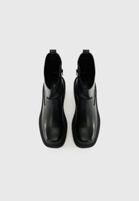 Bottines en cuir noir avec une texture lisse, bout carré et fermeture éclair sur le côté. Les semelles présentent un design nervuré pour une meilleure adhérence.