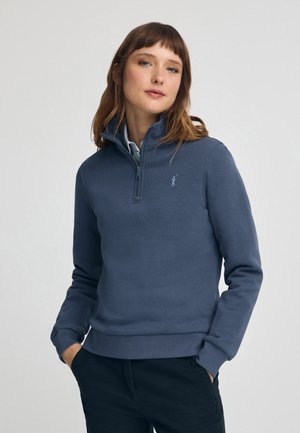 Felpa con zip di un blu scuro, con colletto alto, caratterizzata da un logo sottile sul petto e polsini e orlo a costine.