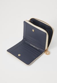 Marineblaue Lederbörse mit goldenem Reißverschluss. Das Innere bietet Kartenfächer, ein Logo-Prägung und einen dekorativen Charm. Glatte Textur und kompaktes Design.