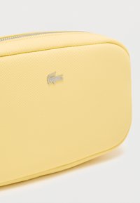 Gul tekstureret lynlåspung med et lille sølv krokodillelogo. Rektangulær form med glatte kanter og holdbart ydre.