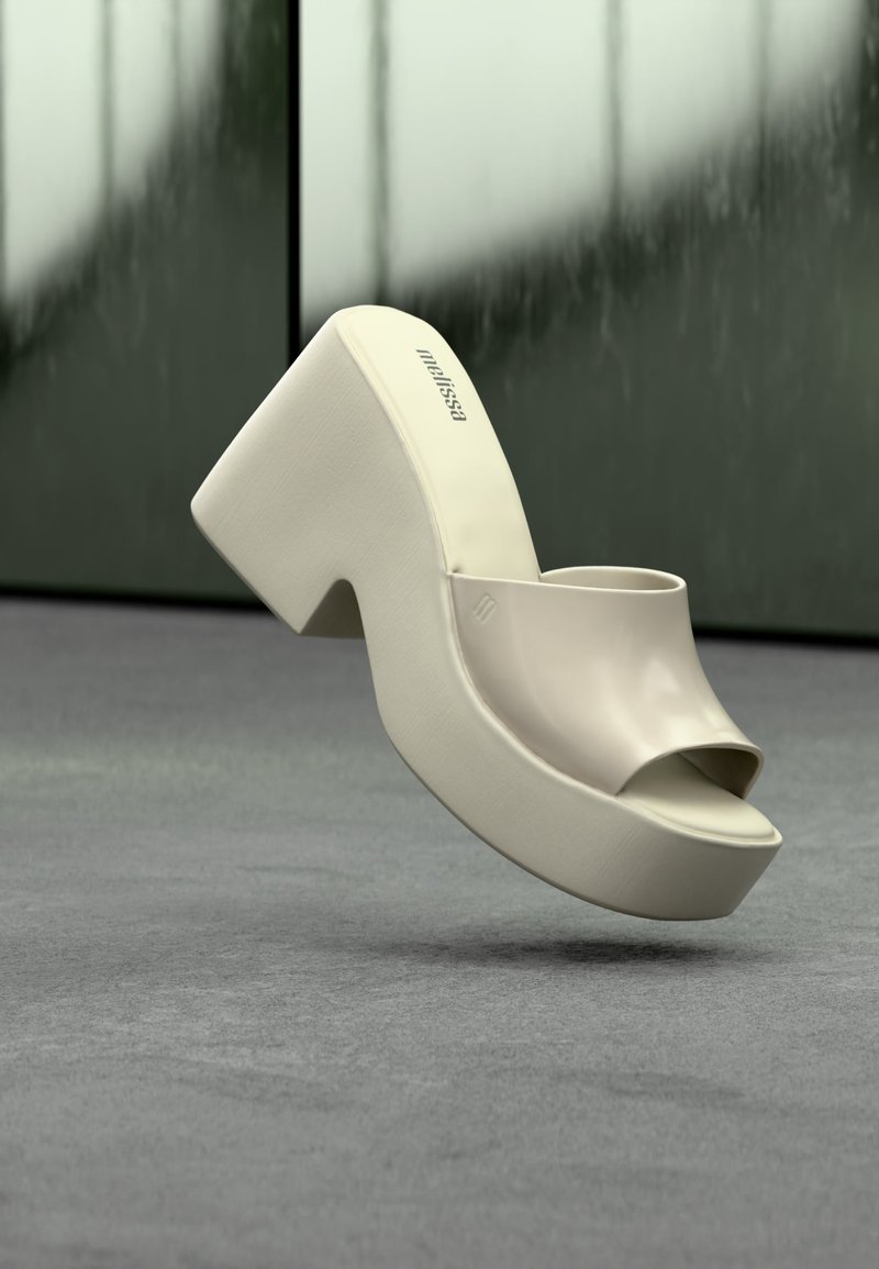 Sandale à plateforme beige avec bout ouvert et talon bloc flottant au-dessus d'un sol gris sur un fond vert flou.