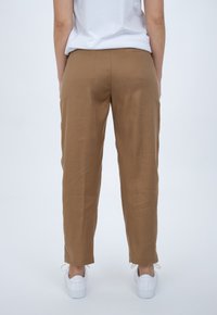 Brown, lightweight trousers with a straight-leg design, smooth texture, and cuffed ankles, paired with white sneakers.