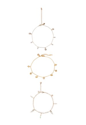 Tre braccialetti delicati con piccoli ciondoli pendenti a forma di conchiglie, cristalli, cuori e foglie, disposti verticalmente su uno sfondo bianco.