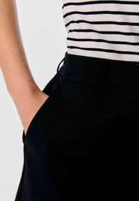 Zwarte broek met een zijzak, gecombineerd met een gestreepte ribbeltop. De stof lijkt glad met een aansluitend ontwerp rond de taille.