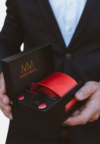 Corbata de satén rojo en una caja negra de regalo con acentos plateados. La caja presenta el logo dorado "MASSI MORINO" en la tapa interior.