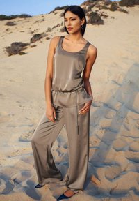 Satin grijze outfit met een mouwloze top met een peplum taille en wijdvallende broek, geaccentueerd met een zilveren kettingriem en puntige marineblauwe schoenen.