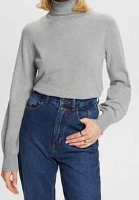 Pull à col roulé gris à manches longues, fabriqué en matière douce. Associé à un jean en denim bleu taille haute. Design simple, sans motifs.