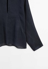 Blouse en lin bleu marine foncé à manches longues, avec une ouverture en forme de trou de serrure à l'avant et un ourlet légèrement arrondi. Tissu texturé avec une coupe décontractée.