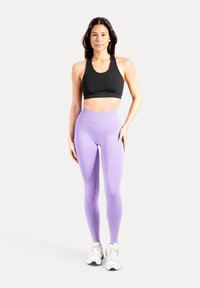 Zwarte sportbeha met een racerback-ontwerp, gecombineerd met lichtpaarse leggings met hoge taille, voorzien van een gladde textuur en naaddetails. Witte sportschoenen.