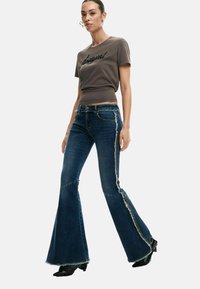 Hall halli puuvillane T-särk tikitud tekstiga, sobitatud siniste flared teksadega, millel on lõhenevad küljesõmblused ja tavaline vöökoht. Mustad kontsaga saapad.