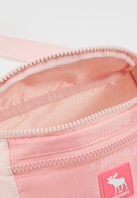 Różowe wnętrze materiałowej torby z zamykaną na zamek kieszonką, gładką teksturą i metką z logo łosia. Wyściełane dopasowanym różowym materiałem.