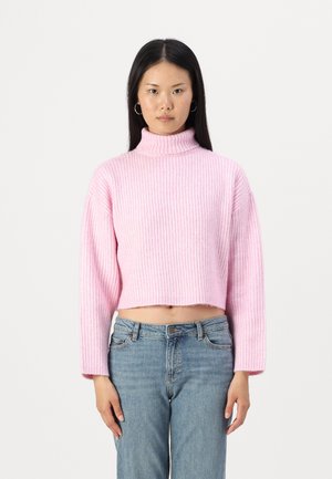 Pink ribbed cropped turtleneck sweater with long sleeves, featuring a textured knit pattern. Worn with light blue high-waisted jeans.