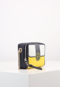 Zippered handbag featuring a structured shape, made of yellow and navy synthetic material, with gold chain accent and logo detail.