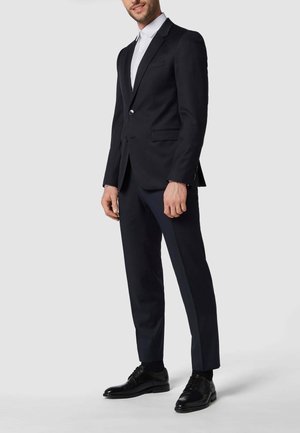 Marineblauer Anzug mit einreihigem Blazer, glatten Vorderhosen und einem weißen Hemd, ergänzt durch polierte schwarze Schnürschuhe.