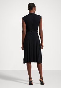 Černé šaty bez rukávů s přiléhavým živůtkem, rozšířenou sukní a páskem v pase. Hladká, elastická látka s vysokým výstřihem a zadním zipem.