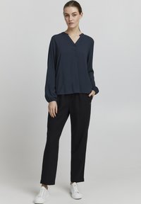 Blusa de manga larga azul marino con escote en V y tapeta de botones, combinada con pantalones negros holgados y zapatillas blancas. Tejido suave, corte relajado.