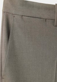 Gros plan d'un pantalon en tissu gris montrant la ceinture, les passants de ceinture et la couture de la poche latérale.