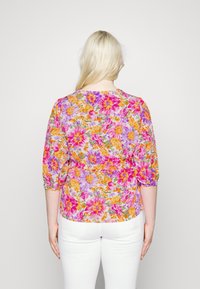 Blouse à imprimé floral avec des manches trois-quarts. Présente des fleurs vibrantes de couleur rose, violette et orange sur un fond clair. Tissu léger.