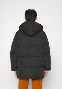 Svart boblejakke med hette, med quiltet design, lange ermer og glidelås, som går ned til midten av lårene.