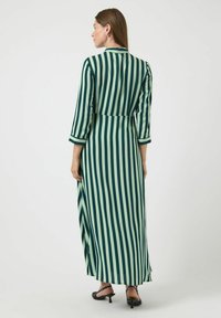 Maxi šaty ve tmavě zelené a světle zelené svislé pruhy, s tříčtvrtečními rukávy, límečkem a vysokým rozparkem na sukních.