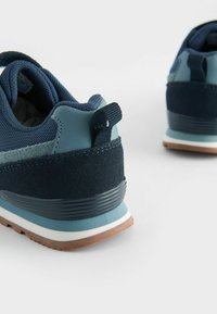 Mörkblå sportskor med en blandning av mesh och mocka material, en texturerad bakdel och en kontrasterande ljusblå och vit sula.