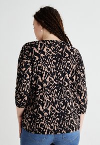 Svart och beige djurtryckstopp med trekvartslånga ärmar, rund halsringning och mjuk textur, kombinerat med blå jeans.