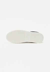 Sneaker nera con una toma in tela testurizzata e una suola in gomma bianca caratterizzata da un motivo rigato. Logo impresso sul lato della suola.