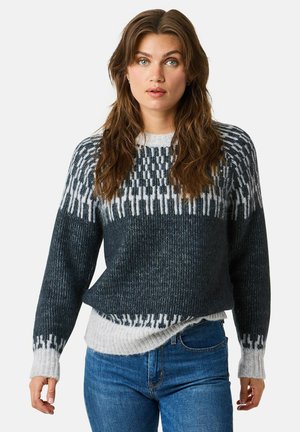 Knit sweater in dark gray and white with a geometric pattern on the yoke, loose fit, and ribbed cuffs, layered over a lighter sweater.