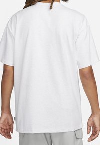 Vit bomullströja med en avslappnad passform, korta ärmar, rund halsringning och en etikett nederst. Tyget ser mjukt ut med en slät textur.