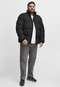 Sort puffjakke med høj krave, med quiltede sektioner. Parret med lys grå bukser og mørke sneakers. Casual, afslappet pasform.