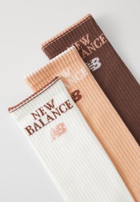 Drei Paar gerippte Socken in Weiß, Pfirsich und Braun, jeweils mit dem „NEW BALANCE“-Logo in kontrastierenden Farben am Bündchen.