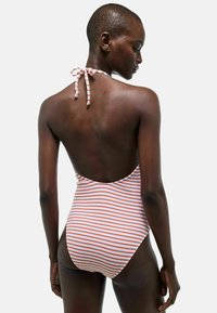 Maillot de bain une pièce rayé en blanc et orange, avec un dos nu et un col tie halter. Texture douce et finition lisse.