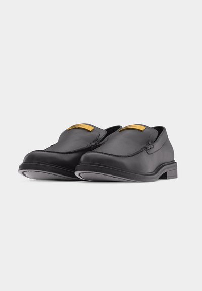 Μαύρα δερμάτινα loafers χωρίς κορδόνια με χαμηλά τακούνια και χρυσές ορθογώνιες λεπτομέρειες στο πάνω μπροστινό μέρος κάθε παπουτσιού.