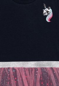 Granatowa koszulka z cekinowym wzorem jednorożca, wyposażona w srebrny, brokatowy pas oraz różową, teksturowaną spódnicę z tiulu z kolorowymi plamkami.