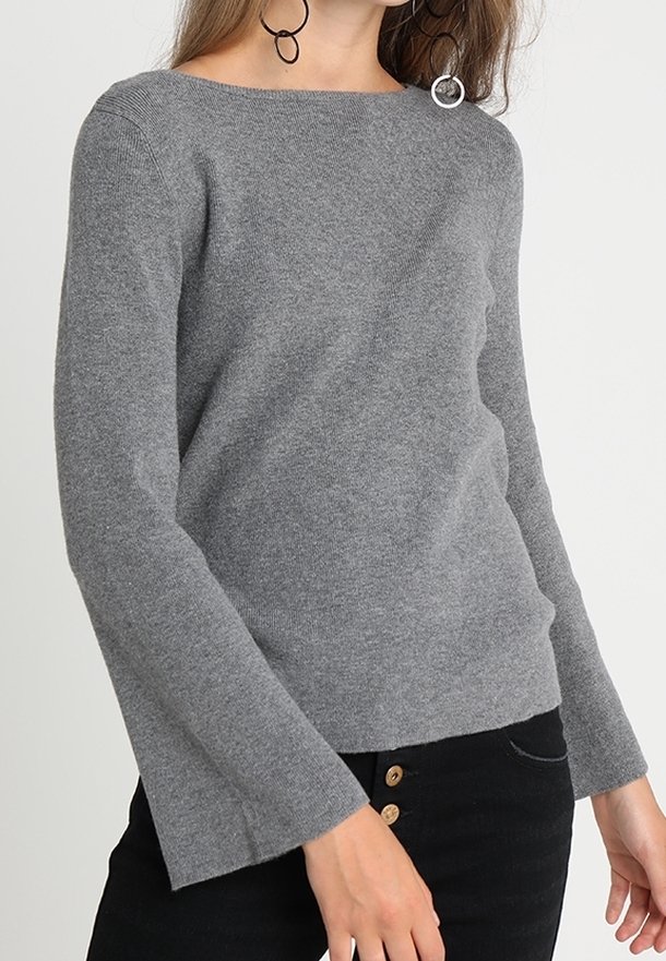 Grå strikket sweater med bådudskæring, lange klokkeærmer og en afslappet pasform. Et par knapper synlige på sorte bukser.