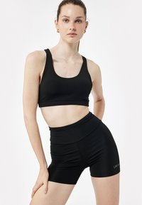 Musta urheiluliivi, jossa on kaarroke kaula-aukko ja korkeavyötäröiset shortsit, jotka on valmistettu teksturoidusta joustavasta kankaasta; shortseissa on huomaamaton brändilogo.