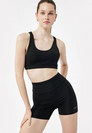 Musta urheiluliivi, jossa on kaarroke kaula-aukko ja korkeavyötäröiset shortsit, jotka on valmistettu teksturoidusta joustavasta kankaasta; shortseissa on huomaamaton brändilogo.