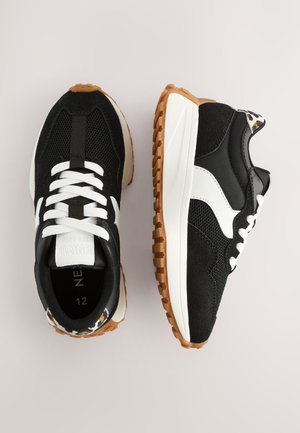 Melni sporta apavi ar tīkla un zamšādas materiāliem, baltām šņorēm, gumijas zolīti un rakstainu papēža detaļu. Izmērs 12.